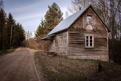 Cottage by dirt road against sky