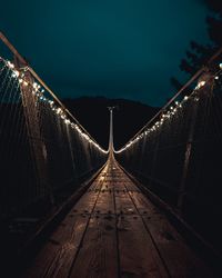 Illuminated footbridge against sky at night