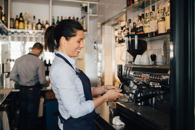 Smiling barista using coffee maker in restaurant