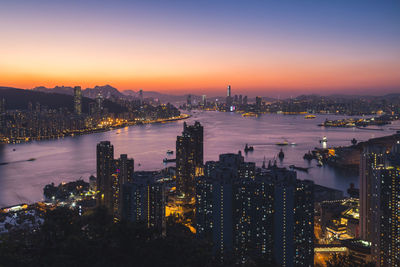 High angle view of illuminated buildings by river at dusk