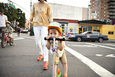 Portrait of boy riding push scooter with family on streets in city