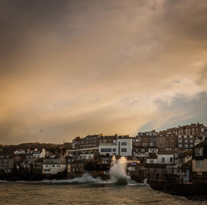 Waves splashing on shore by residential district against cloudy sky