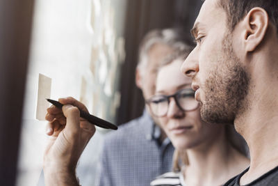 Side view of businessman writing on adhesive note in office