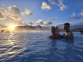 Rear view of woman swimming in sea against sky during sunset