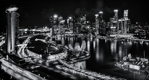 Illuminated skyscrapers by bay against sky at night