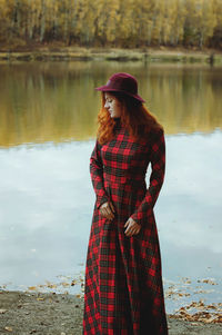 Redhead elegant woman in red dress and hat walking in autumn park.