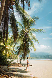 Side view of unrecognizable female in swimwear enjoying summer holidays on picturesque seashore with tropical palms and sandy beach in uvita town in costa rica