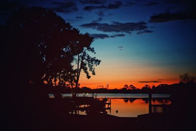 Silhouette trees by lake against sky at sunset