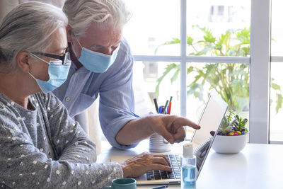 Senior couple wearing flu mask working on laptop at home