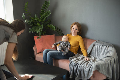 Happy grandmother holding baby grandson on sofa at home living room