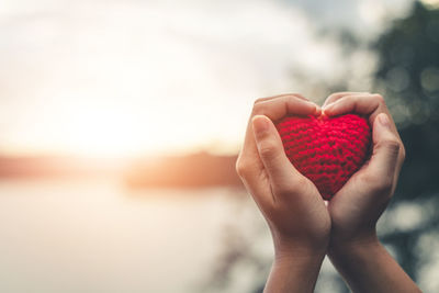 Midsection of woman holding heart shape against sky