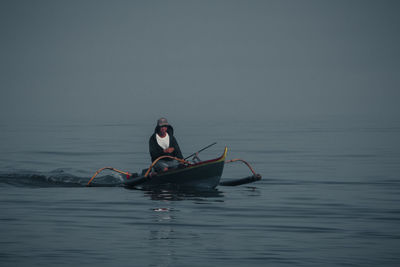 Man rowing boat in sea against sky