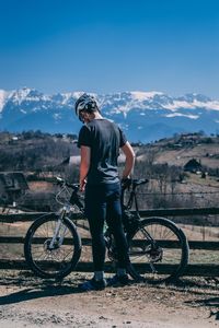 Man standing with bicycle on mountain against sky