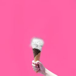 Close-up of hand holding ice cream against pink background
