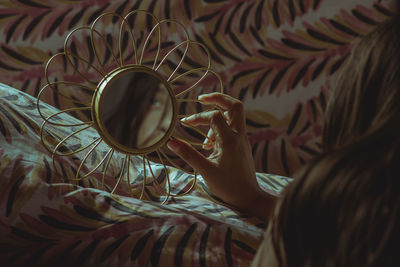 Close-up of woman holding mirror lying on bed