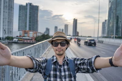 Portrait of young man wearing sunglasses against buildings in city