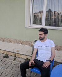 Young man looking down while sitting against window