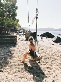 Shirtless girl sitting on swing at beach