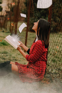 Side view of young woman holding paper outdoors