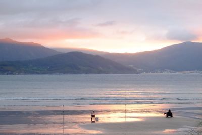 People on beach against sky during sunset