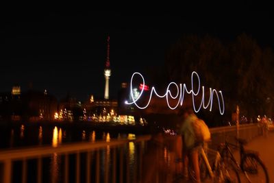 Blurred motion of man by illuminated city against sky at night