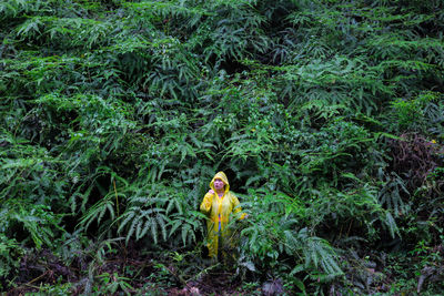 Woman wearing raincoat while standing amidst plants during rainy season