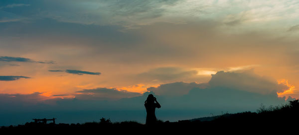 Silhouette woman standing on field against cloudy sky during sunset
