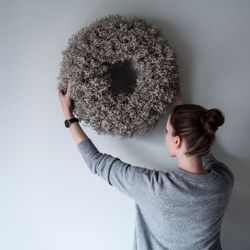 Rear view of woman placing wreath decoration on wall at home