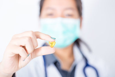 Female doctor holding heart shape pill against white background