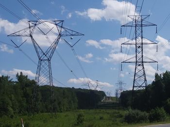 Electricity pylon by trees against sky