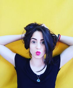 Close-up portrait of beautiful woman puckering lips with hands in hair by yellow wall