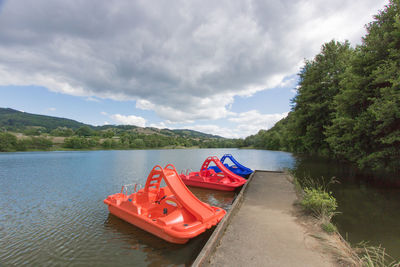 Red boat moored on lake against sky