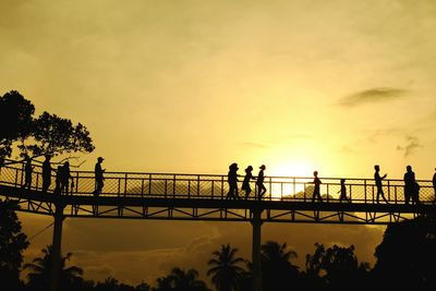 Silhouette people on bridge against sky during sunset