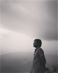 Side view of man looking at mountain against sky