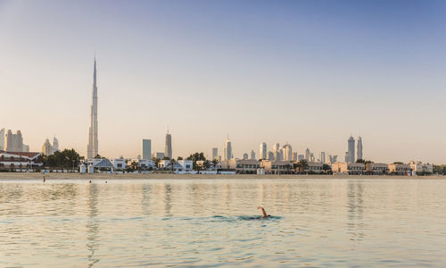 Modern buildings by sea against clear sky during sunset