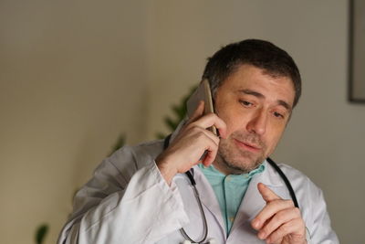 Close-up of mature doctor using phone against wall