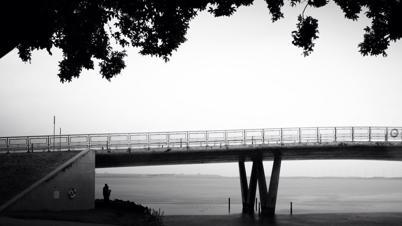 connection, water, bridge - man made structure, bridge, tree, clear sky, tranquility, built structure, river, sky, sea, railing, tranquil scene, nature, copy space, architecture, engineering, transportation, silhouette, scenics