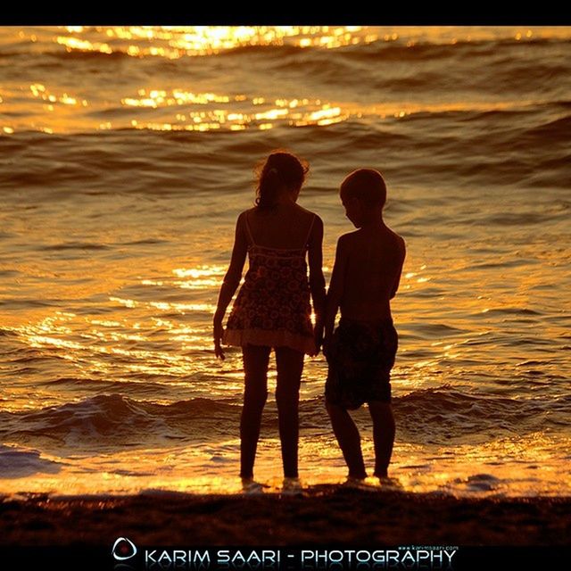 water, lifestyles, sea, sunset, leisure activity, men, togetherness, silhouette, love, standing, bonding, beach, rear view, person, shore, full length, vacations, friendship