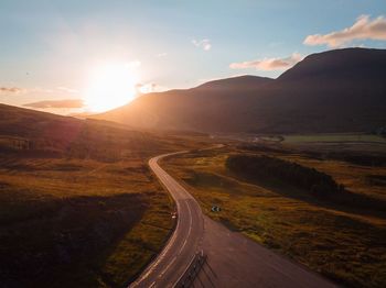 Road leading towards mountains against sky during sunset