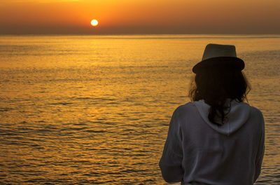 Rear view of woman standing by sea against sky during sunset