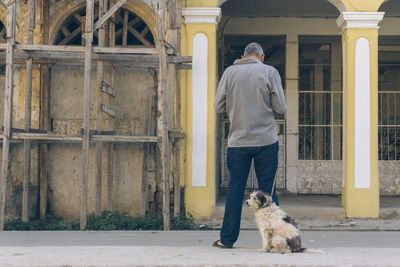 Rear view of man with dog standing outside house