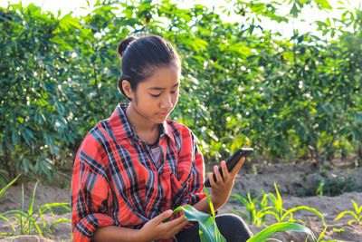 Young man using mobile phone while sitting on plant