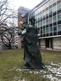 Statue by bare tree against building in city