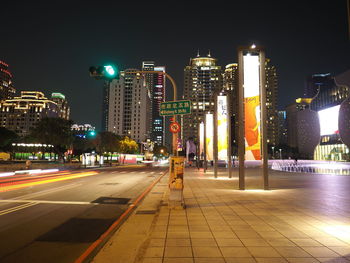 Illuminated street amidst buildings against sky at night