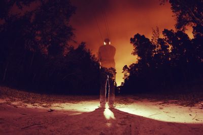 Silhouette man standing by trees against sky at night