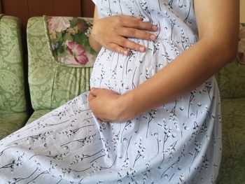 Midsection of woman holding white while sitting at home