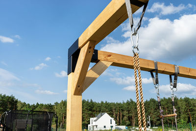 A modern cubic playground made of wooden logs and metal corners, visible nylon ropes and clip hook.