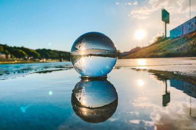 Close-up of crystal ball on lake against blue sky