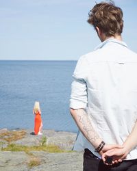 Rear view of friends standing on sea shore against clear sky