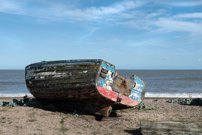 Abandoned boat on beach against sky